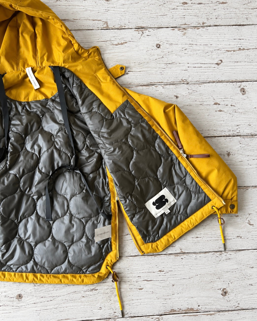 Supermoon Field Parka in Arrowwood yellow, product image 7. Showing close up of jacket internals showing contrast onion stitch quilting and internal shoulder straps 